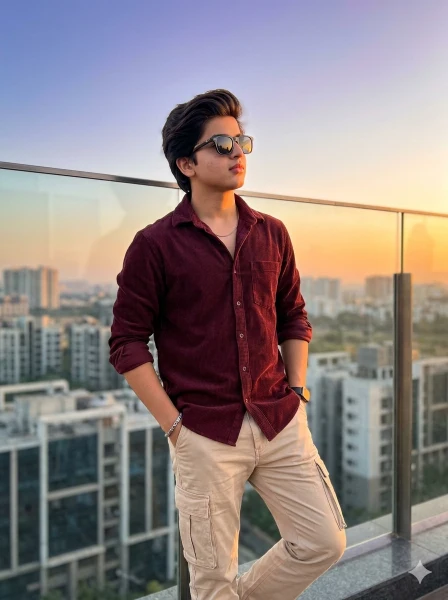 Ultra-realistic young Indian man standing on a modern rooftop terrace during golden hour sunset, wearing a maroon corduroy shirt and beige cargo pants